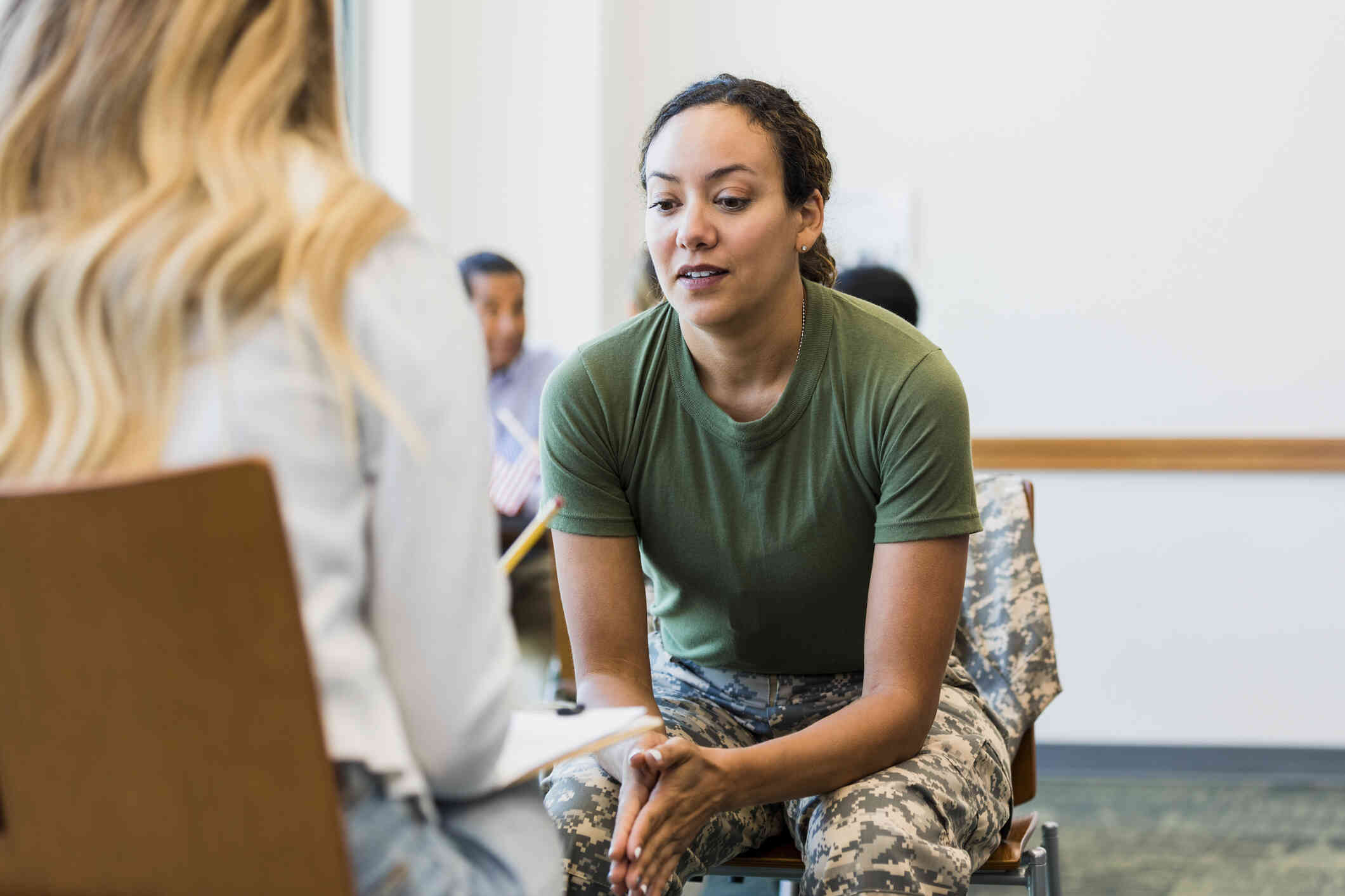 A woman in a military uniform leans forward  in her chair and listens to her female therapist talk.